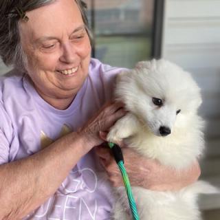 A smiling woman holding a fluffy white puppy outside.
