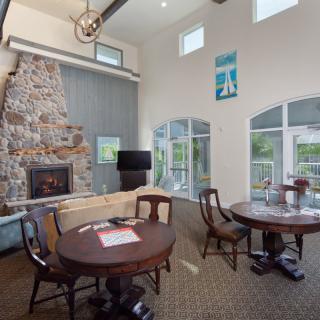 A cozy living room with a stone fireplace, tables, and chairs near large windows.