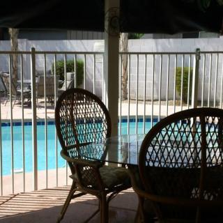 Outdoor patio area with chairs overlooking a fenced pool on a sunny day.