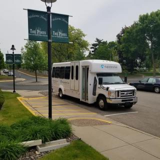 A shuttle bus parked in a lot near green trees and signage on an overcast day.