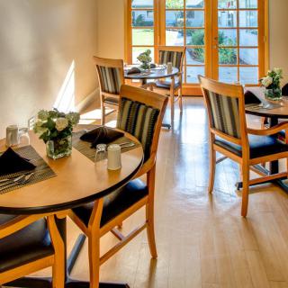 A cozy restaurant dining area with wooden tables and chairs, well-lit by natural light.