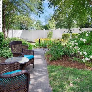 A tranquil garden with a cozy outdoor seating area and a pathway surrounded by lush greenery.