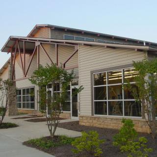 A modern library building with large windows surrounded by greenery.