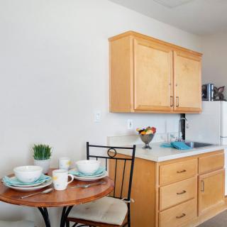 A small kitchen area featuring wooden cabinets, a compact dining table set with plates and cups.