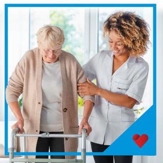 A caregiver assists an elderly woman using a walker.