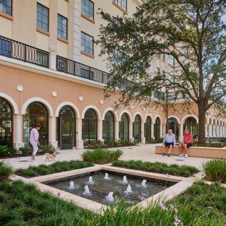 A beautiful courtyard with a fountain surrounded by a landscaped garden and an elegant building.
