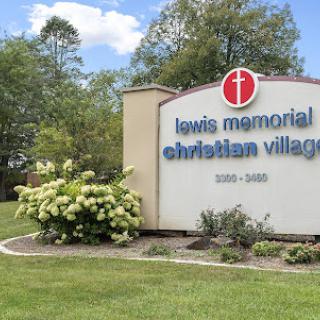 Entrance sign of Lewis Memorial Christian Village surrounded by lush greenery.