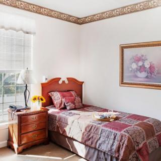 A cozy bedroom with a single bed, adorned with a patterned quilt and lit by natural sunlight streaming through the window.
