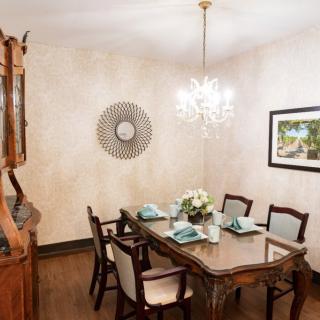 Elegantly set dining room with a classic wooden table and chairs, illuminated by a chandelier.