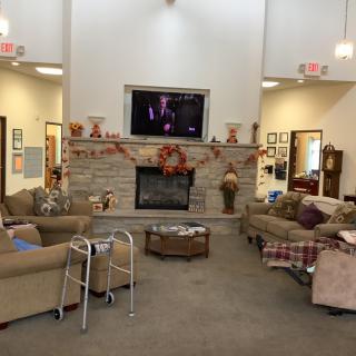 A cozy communal living room with a fireplace, television, and seating, decorated with fall-themed ornaments.