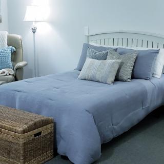 A cozy bedroom with blue bedding and a wicker chest at the foot of the bed.