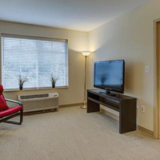 A minimalist living room with a TV, red chair, and floor lamp near a window.