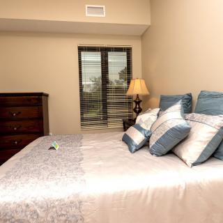 A cozy bedroom with a neatly made bed, decorative pillows, and a bedside lamp.