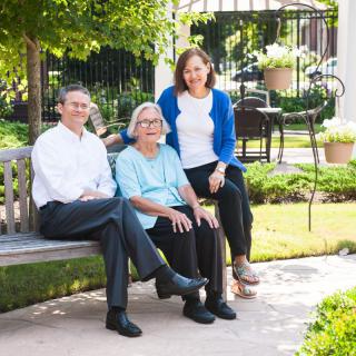 A family sitting on a bench in a garden, enjoying the outdoors together.