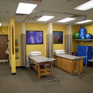 A physical therapy clinic room featuring treatment tables, exercise balls, and bright yellow walls.