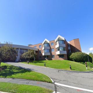 A brick residential building with a well-maintained lawn and trees, situated in a suburban area.