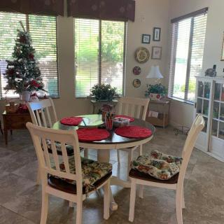 A cozy dining room with a round table set for four, featuring holiday decorations and a small Christmas tree by the window.