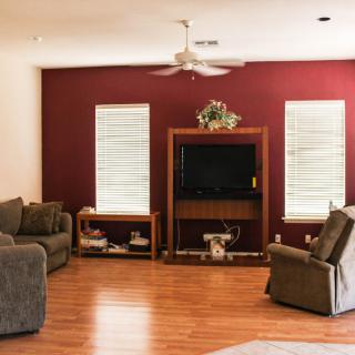 A cozy living room with a red accent wall, featuring a television, sofas, an armchair, and wooden flooring.