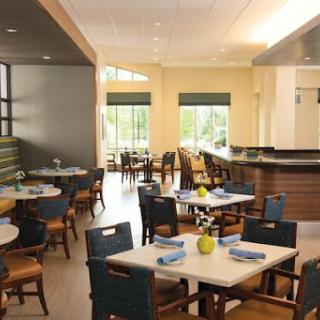 A bright and modern dining area featuring simple wooden tables and comfortable chairs, illuminated by natural light.