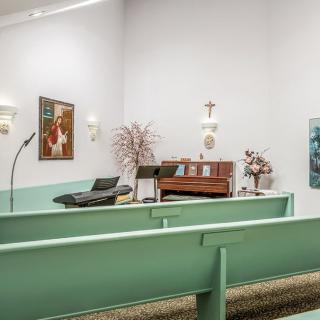 A small chapel with mint green pews and an organ, adorned with religious symbols and decor.