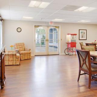 A well-lit room with wooden flooring, featuring chairs, a table, and a popcorn machine near the doorway.