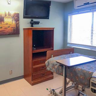 A well-equipped hospital room featuring a bed, television, and a wooden cabinet.