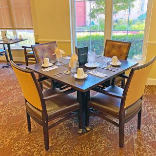 A neatly set dining table in a restaurant interior with four chairs and place settings.