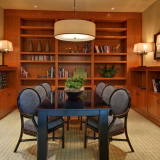 A modern dining room with a sleek table, upholstered chairs, and built-in bookshelves.