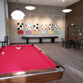 A modern billiard room with a red pool table and contemporary art on the walls.