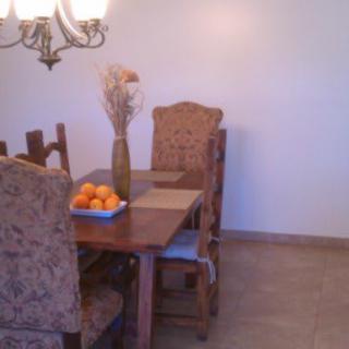 A cozy dining room with a wooden table set, adorned with a fruit bowl and a decorative vase.