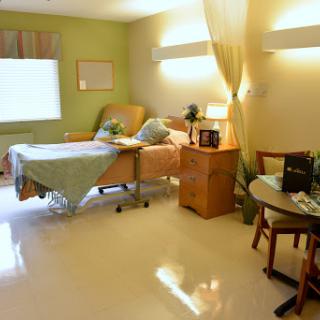 A well-lit hospital room featuring a patient bed, bedside table, and seating area.