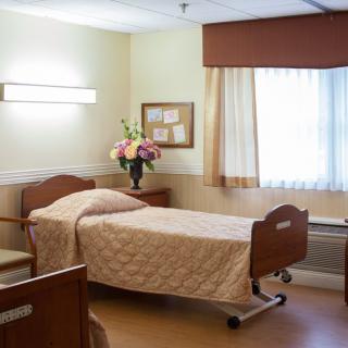 A hospital room with a neatly made bed and floral arrangement.