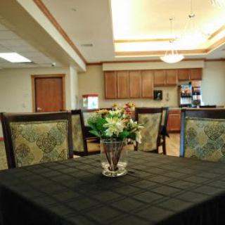 A cozy dining area with a table and chairs, featuring a floral centerpiece and an adjacent kitchen.