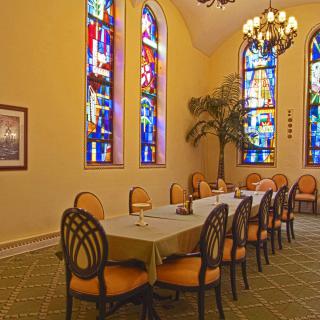 A dining room featuring a long table surrounded by chairs, adorned with stained glass windows and a chandelier.