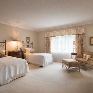 A spacious and elegantly decorated bedroom featuring two beds, a large window with drapes, and tasteful furniture in neutral tones.