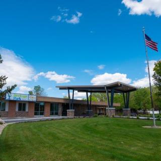 A modern building with a flagpole and a well-maintained lawn under a clear blue sky.