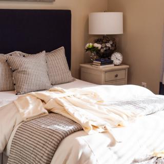 A cozy bedroom with a neatly made bed, pillows, and a nightstand featuring a lamp and decorative items.