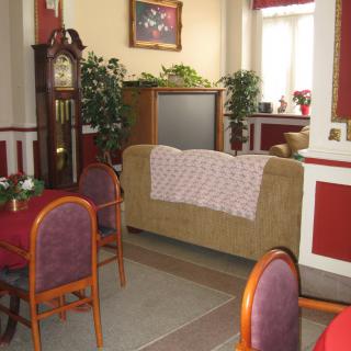 A cozy living room with a sofa, dining chairs, and a grandfather clock in a red and beige color scheme.