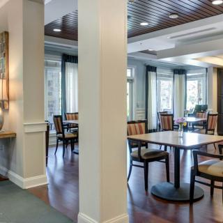 A modern dining area with tables and chairs, featuring large windows and wooden flooring.