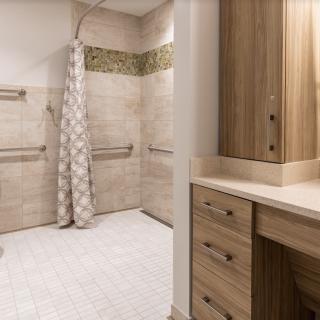 A modern bathroom features a spacious shower area with patterned tiles and grab bars, alongside wooden cabinets for storage.
