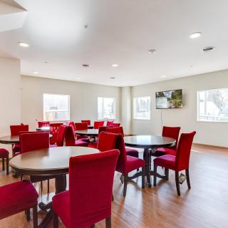 A modern dining area with red chairs and round tables, featuring large windows and a wooden floor.