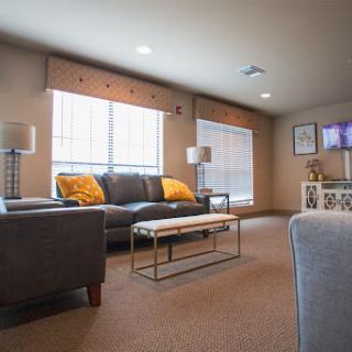 A cozy living room featuring a dark sofa and a glass coffee table, illuminated by natural light from large windows.