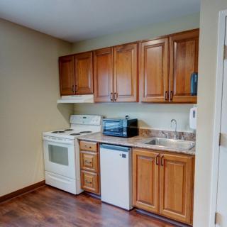 A compact kitchen with wooden cabinets, equipped with a stove, microwave, small fridge, and sink.