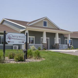 A residential building with a well-maintained lawn and a sign out front on a sunny day.