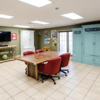 A modern conference room with a wooden table, red chairs, TV, and storage cabinets.