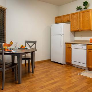 A cozy kitchen and dining area with wooden cabinets, a refrigerator, dishwasher, and a small dining table.