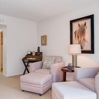 A cozy living room featuring neutral-colored armchairs, a lamp, and artistic wall decor.