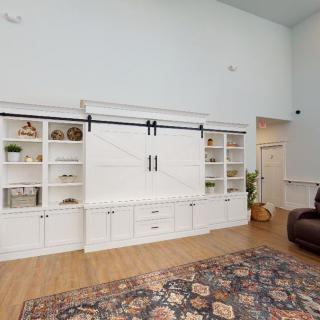 A spacious living room with white bookshelves and a cabinet featuring sliding doors, complemented by wood flooring and an area rug.