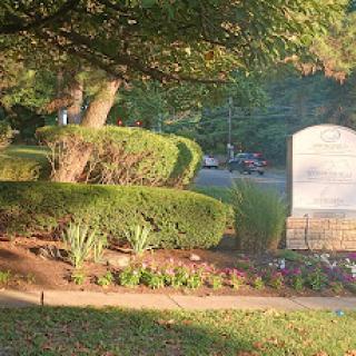 A peaceful cemetery setting with well-maintained hedges and flower beds, bathed in the warm glow of evening sunlight.