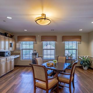 A cozy kitchen and dining area with wooden floors, a round table surrounded by chairs, and large windows letting in natural light.